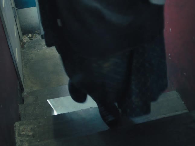 A woman carefully descends a dark and dirty concrete staircase into a basement