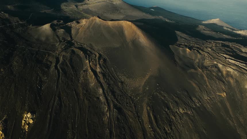 A dramatic timelapse of shadows moving across the dark, barren landscape of the Capelinhos volcano by the sea