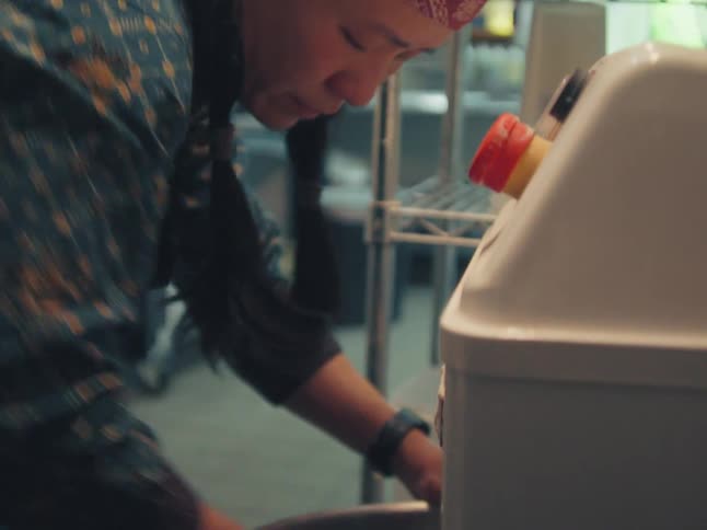 Close up of an Asian baker carefully cleaning the large stainless steel bowl of an industrial mixer in a professional kitchen