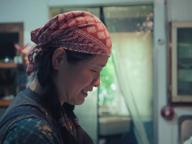A cinemagraph shows an Asian woman in a red bandana smiling happily while working in a warm, cozy setting
