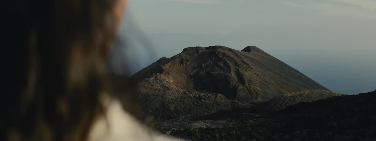 Over-the-shoulder shot of a person looking out at a massive volcanic crater at sunrise