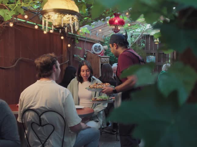 A young couple is happily served their pizza by a waiter while on a date at a charming outdoor patio restaurant