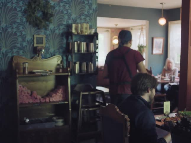 A waiter clears a table for a smiling couple in a busy, eclectic restaurant with unique decor