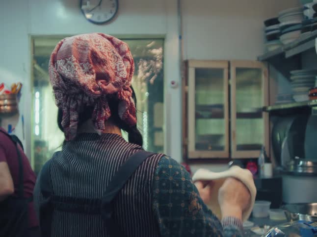 Slow motion shot from behind a female chef as she expertly stretches pizza dough in a professional kitchen