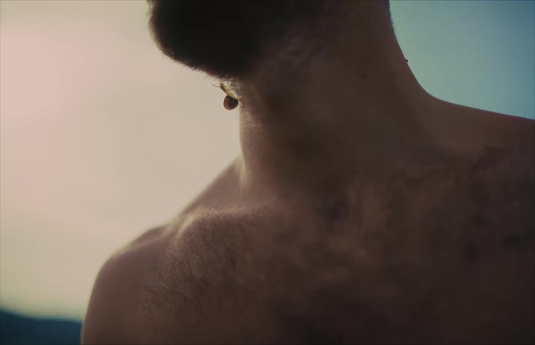 A small snail slowly crawls on the neck of a shirtless man outdoors