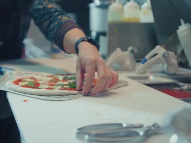 A chef carefully transfers a freshly made margherita pizza onto a metal pizza peel in a professional kitchen