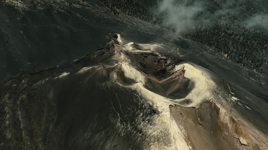 An epic aerial shot reveals the vast, desolate crater of a volcano as thick smoke slowly dissipates