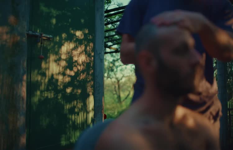 Golden hour light casts dancing tree shadows on a green door as a man receives a relaxing head massage outdoors