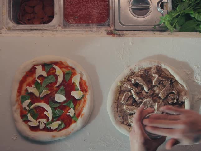 An overhead view shows a chef seasoning a mushroom pizza and then placing it on a peel to be cooked