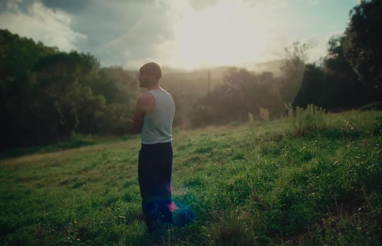 Cinemagraph of a pensive man standing still in a sunlit grassy field