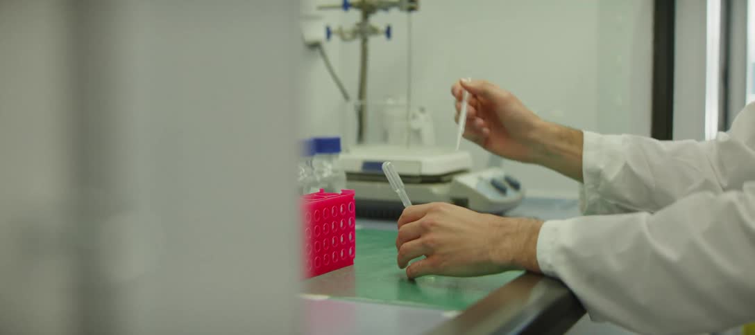 A scientist in a laboratory carefully measures a clear liquid using a pipette and a beaker for a scientific experiment