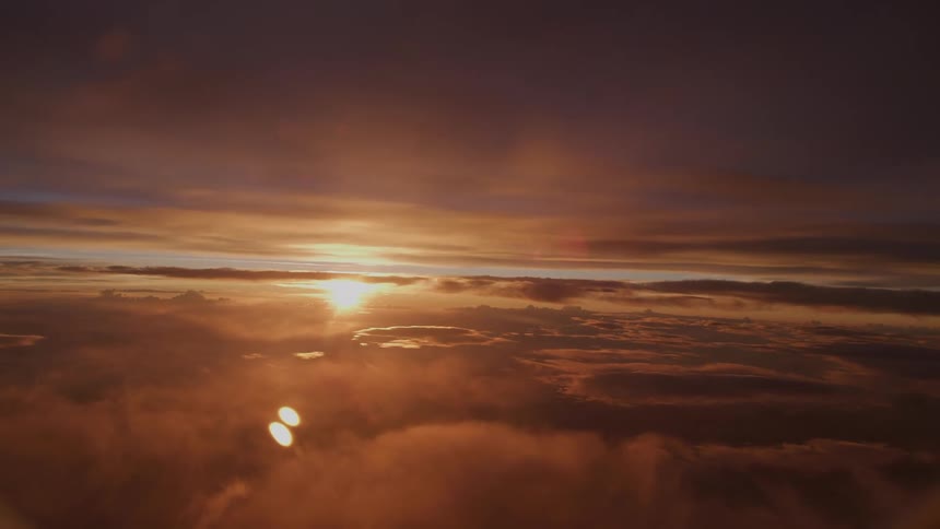 A stunning aerial view captures the golden sun setting over a sea of soft, warm clouds
