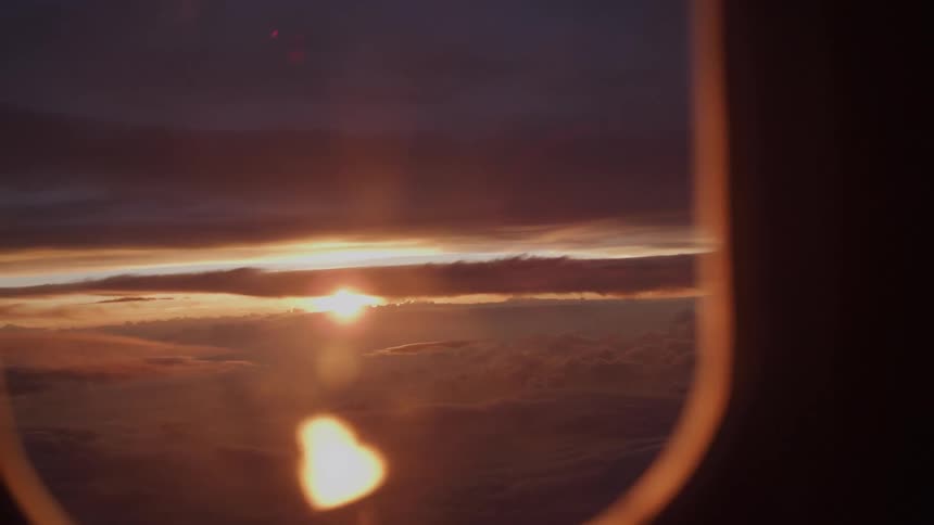 A dreamy view from an airplane window shows a silhouetted hand against a breathtaking sunset over a sea of clouds
