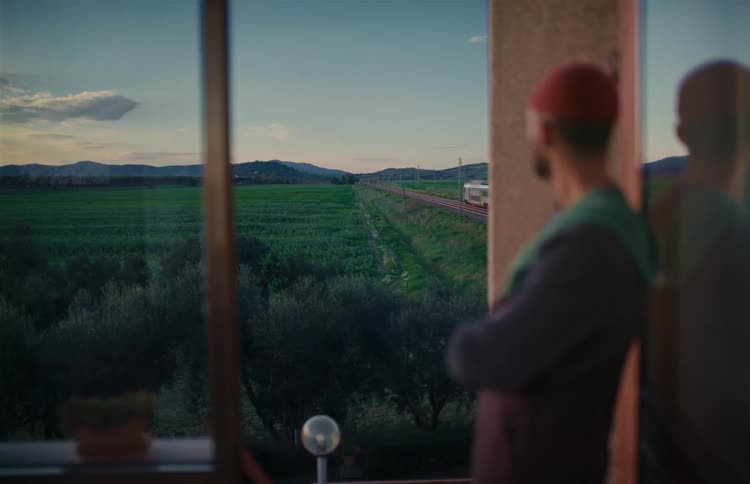 A contemplative man looks out the window as a high-speed train travels through the serene countryside at dusk