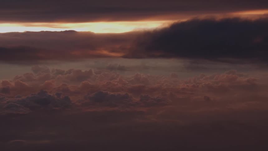 A dramatic aerial view shows a dark and moody cloudscape with a sliver of golden sunset breaking through