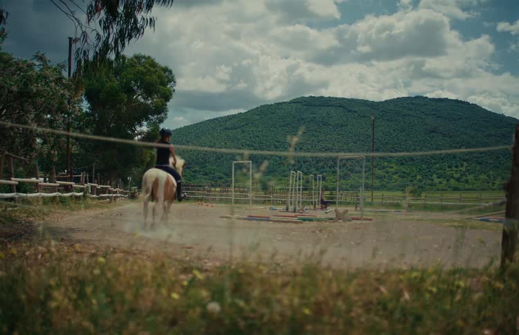 Children and teenagers take horseback riding lessons on ponies at a rural ranch with scenic green hills in the background