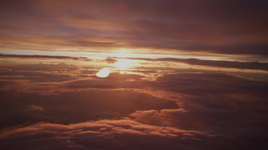 A stunning aerial view captures the majestic beauty of the sun setting over a sea of clouds, painting the sky in warm hues of orange and red