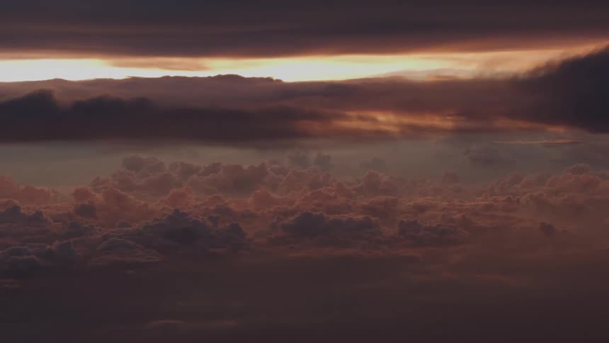 A majestic aerial view shows a vast cloudscape illuminated by the setting sun's golden glow