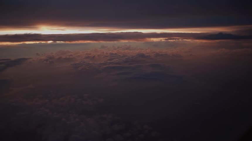 A serene aerial view shows a beautiful, moody sunset casting warm light over a vast sea of clouds