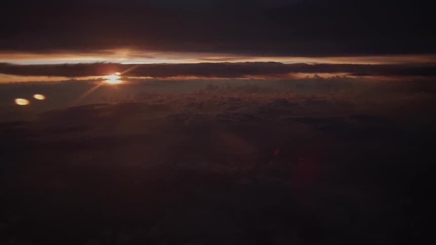 A dramatic aerial view of the sun setting over a vast sea of dark clouds