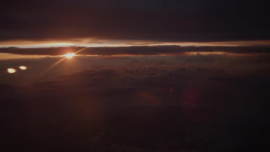 A dramatic sunrise breaks through the dark clouds, casting a golden glow from a high aerial perspective
