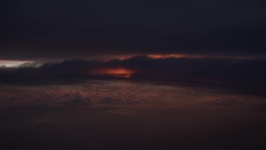 A sliver of orange sunset light breaks through a dark and moody storm cloudscape