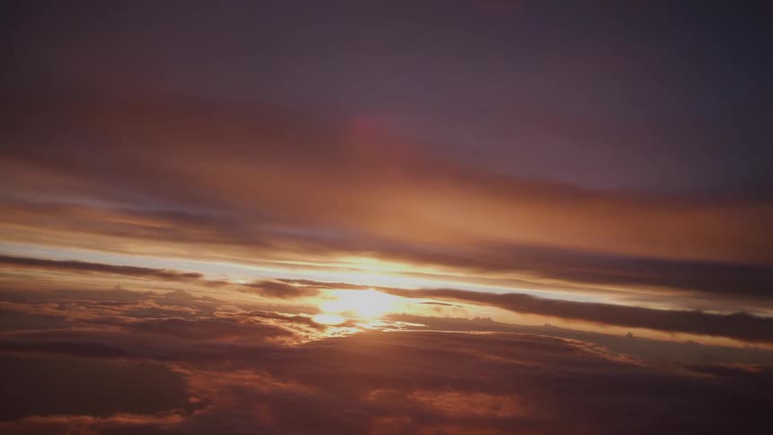 Static aerial view of a vibrant golden and purple sunset over a sea of clouds