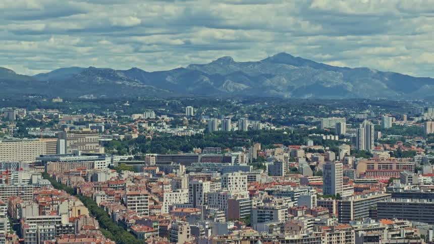 An expansive timelapse of a dense European cityscape with majestic mountains rising in the background under a sky filled with moving clouds