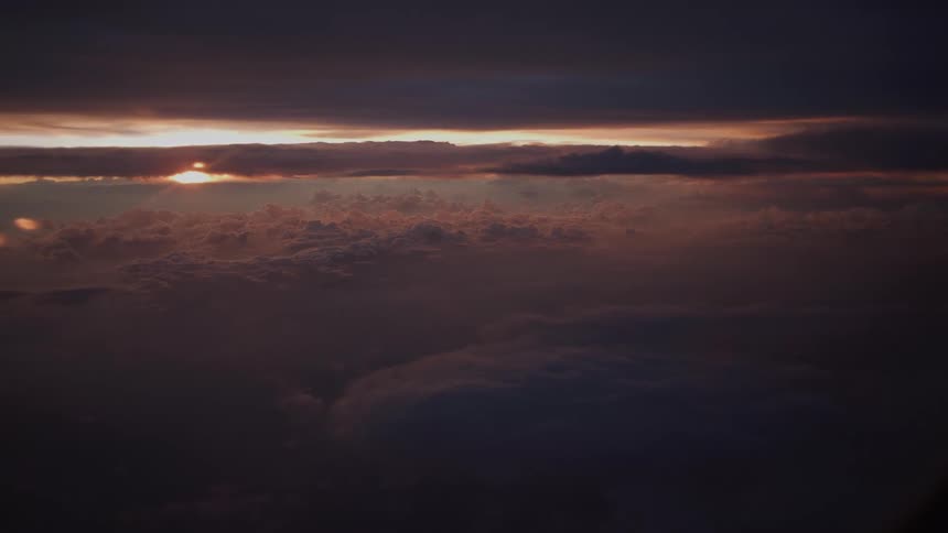 A serene aerial view of a dramatic, moody sunset with the sun peeking through dense layers of clouds