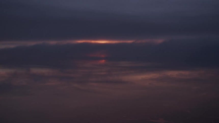 A sliver of the setting sun glows through a narrow gap in dark, ominous clouds at twilight