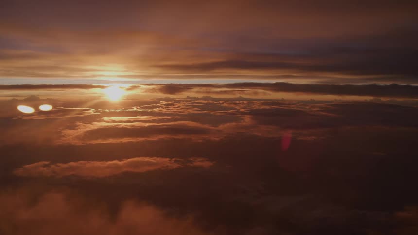 An awe-inspiring aerial view captures the sun setting over a vast sea of clouds, casting a warm, golden glow across the sky