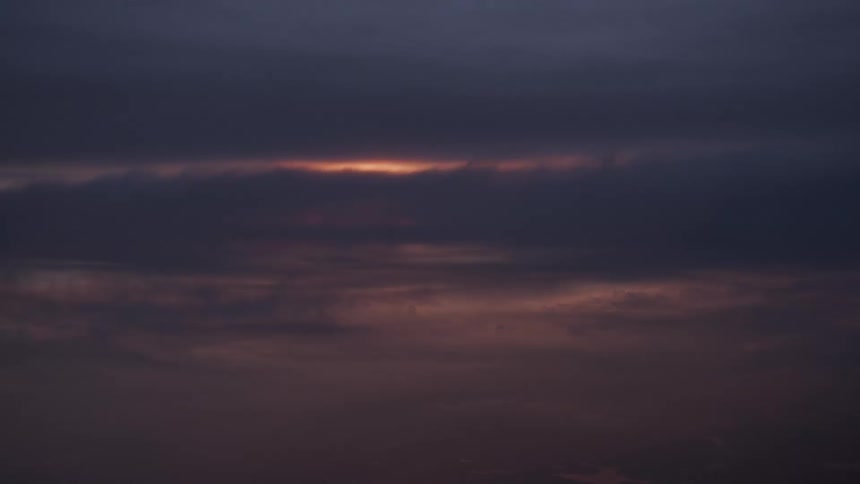 A sliver of the setting sun peeks through dark, ominous clouds during a moody sunset