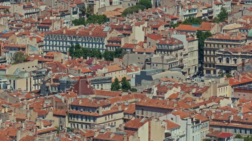 A sunny day timelapse over the dense, historic cityscape and red rooftops of Marseille, France, as shadows shift across the buildings