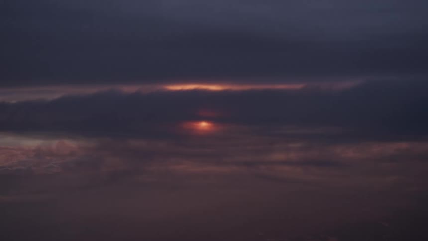 A small, glowing sun sets behind a thick layer of dark, moody clouds