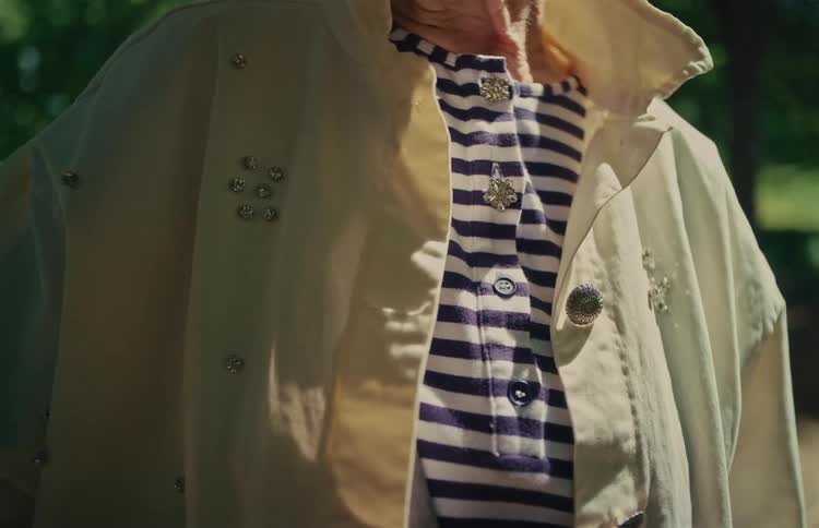 A close-up captures the details of a rhinestone-decorated jacket and a purple striped shirt in the sunlight