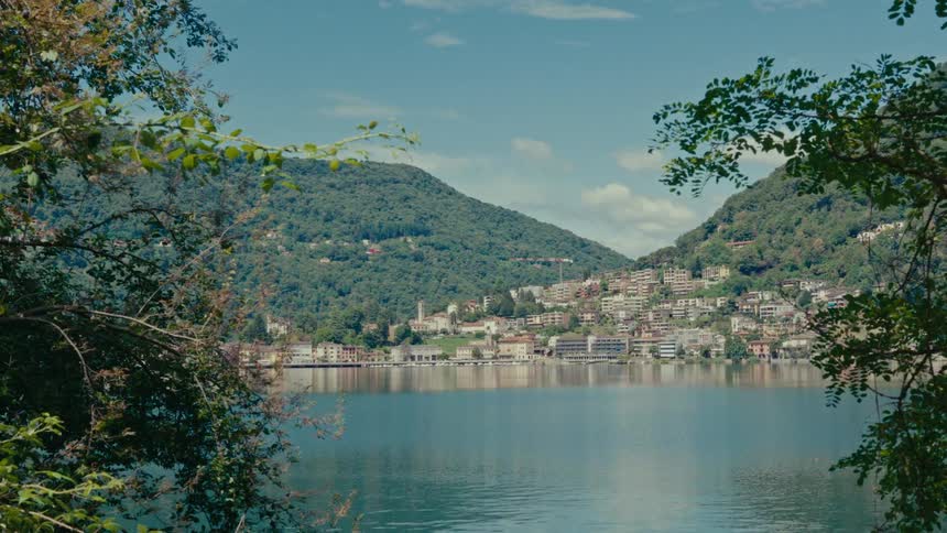 A serene view of a picturesque European lakeside town nestled between lush green mountains on a beautiful sunny day