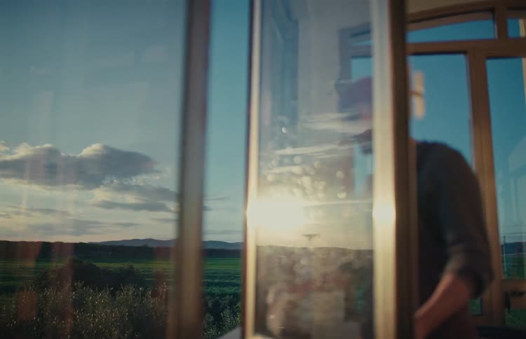 Man cleans a large window revealing a beautiful sunset landscape reflected on the glass