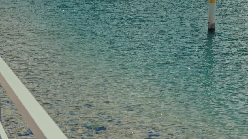 A peaceful, static shot of clear turquoise water shimmering in the sun by a pier