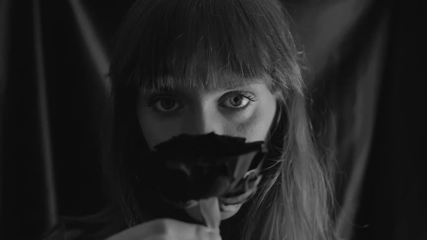 Intense black and white cinemagraph of a mysterious woman holding a dark rose and staring into the camera