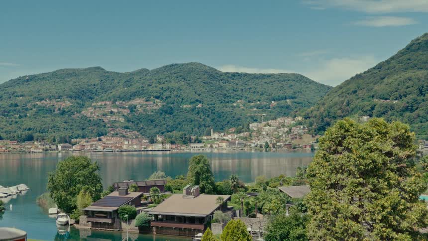 A serene wide shot captures the picturesque lakeside town of Porto Ceresio, nestled against a backdrop of verdant mountains