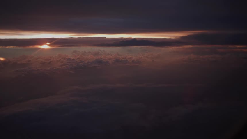 A beautiful and moody sunset over a sea of clouds viewed from an airplane window