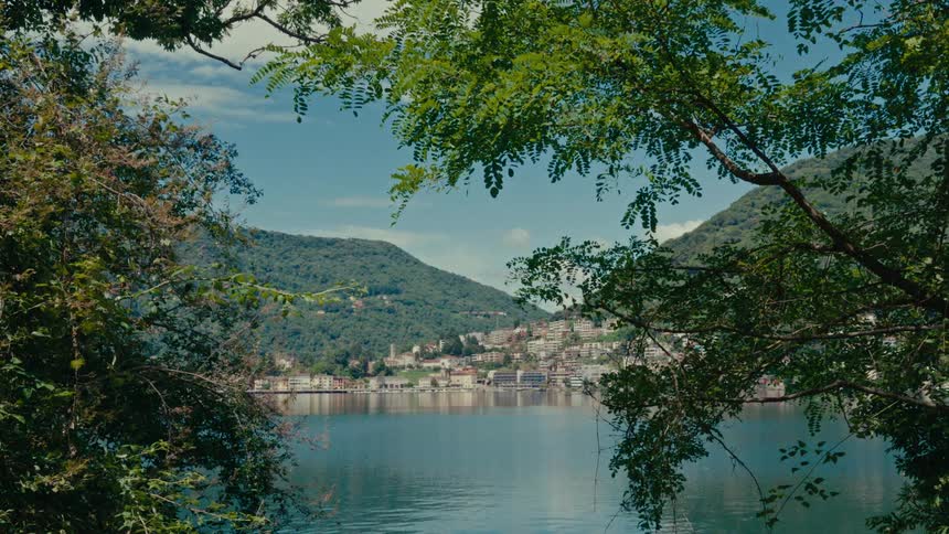 A serene view of a picturesque lakeside town nestled in the mountains, framed by lush green trees