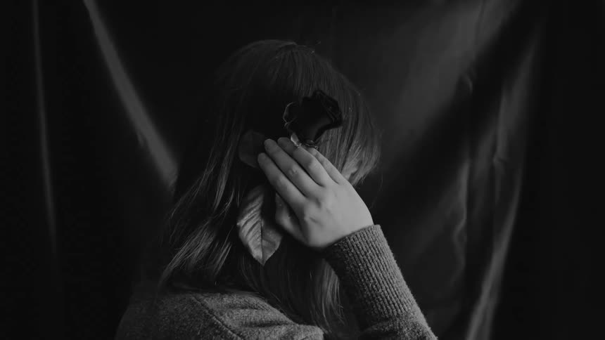 A sad young woman with a rose in her hand turns away from the camera in a dramatic black and white shot