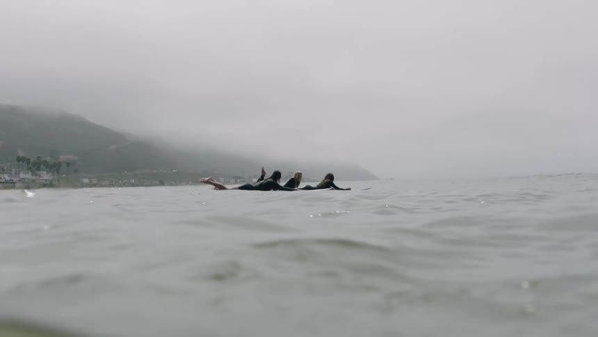 A group of surfers lie on their boards in the calm ocean, waiting for waves on a foggy day