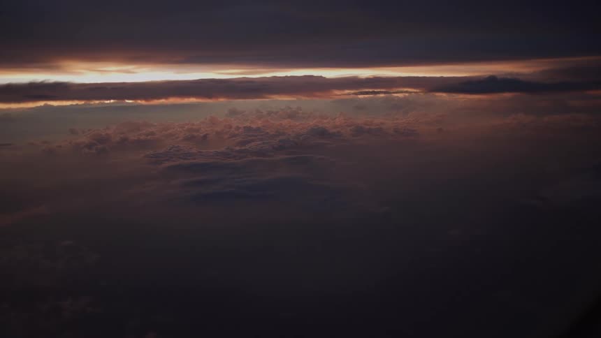 A dramatic aerial view from a plane window captures dark, moody clouds illuminated by the last light of sunset
