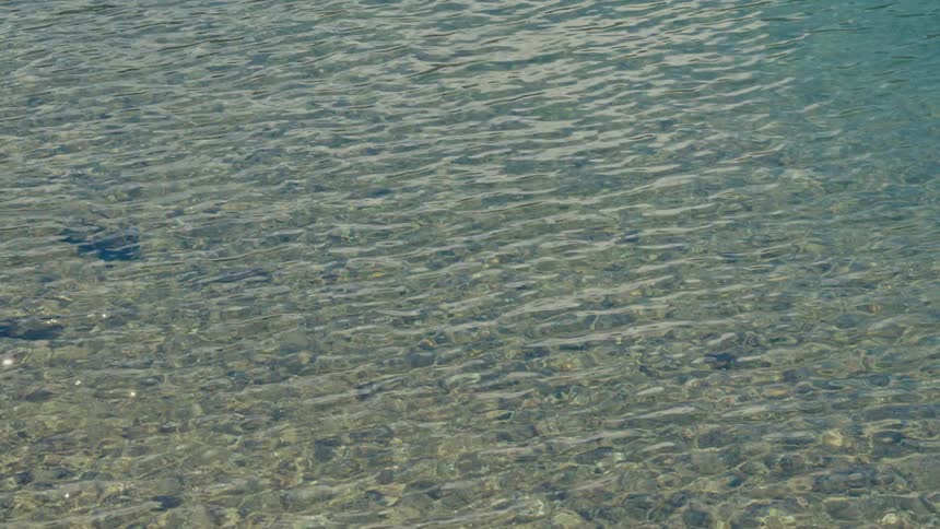 A serene view of crystal clear water with gentle ripples revealing the rocky bottom