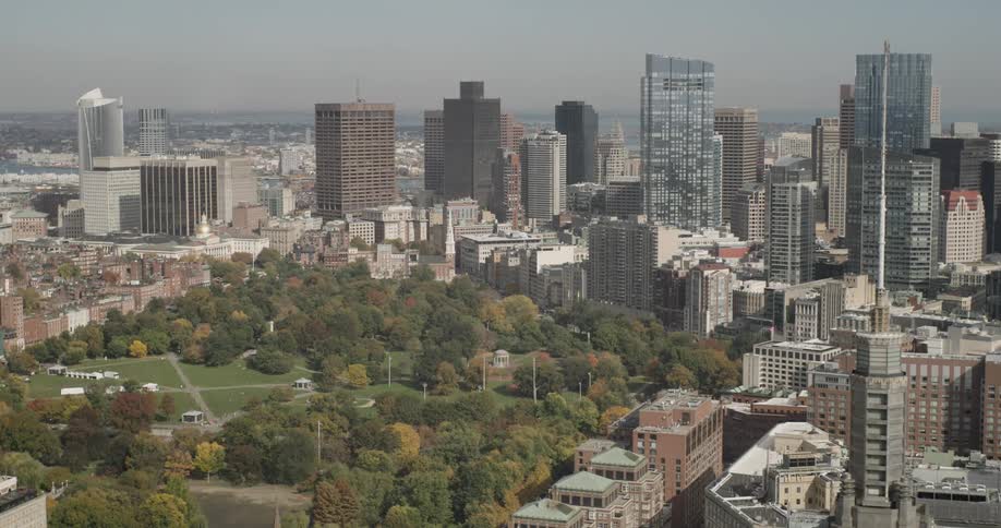 A high-angle static shot of the Boston city skyline with the lush Boston Common park in the foreground during a hazy autumn day