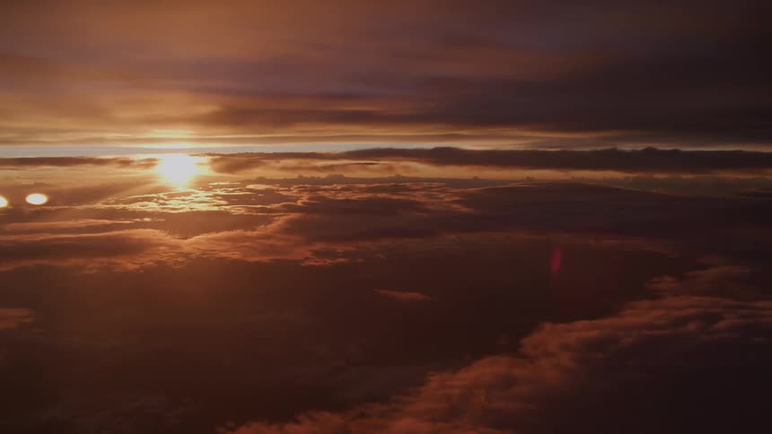 An airplane passenger's view captures a spectacular sunset, with the sun's golden glow illuminating a vast sea of clouds below