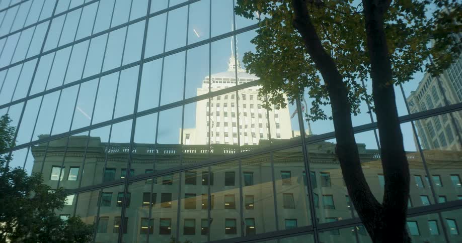 A classic skyscraper is reflected in the windows of a modern glass office building as the camera slowly zooms out