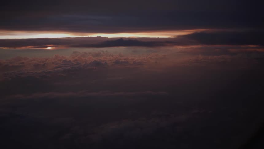 A dramatic aerial view of a dark sea of clouds at sunset with a sliver of light on the horizon